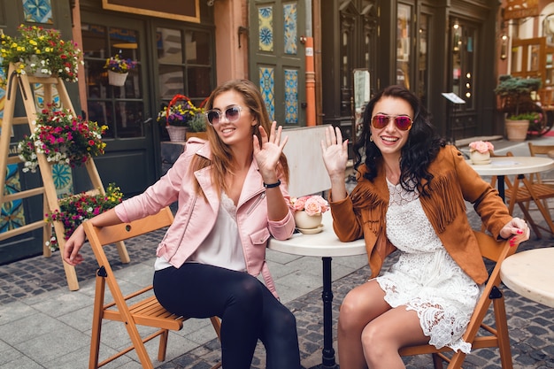 Zwei junge stilvolle Frauen, die am Café sitzen