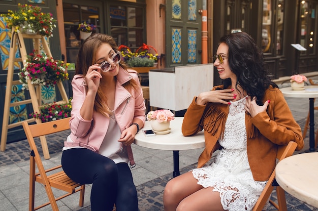 Zwei junge stilvolle Frauen, die am Café sitzen