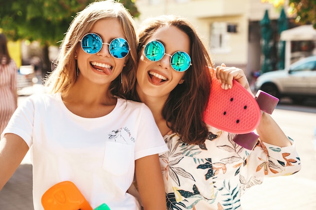 Zwei junge stilvolle lächelnde Hippie-Brünette im sonnigen Sommertag in der Hipster-Kleidung mit Penny-Skateboard-Aufstellung