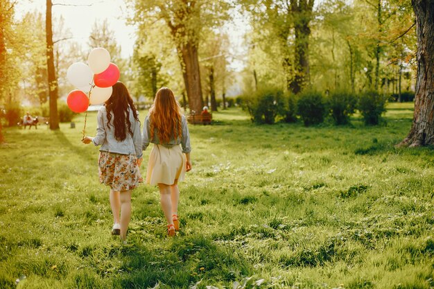 Zwei junge und helle Mädchen verbringen ihre Zeit im Sommerpark mit Ballons