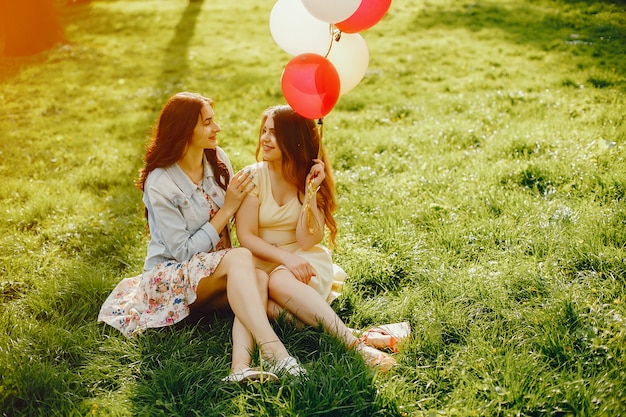 Zwei junge und helle Mädchen verbringen ihre Zeit im Sommerpark mit Ballons