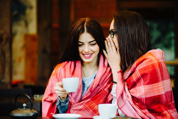 Zwei junge und schöne Mädchen klatschen auf der Terrasse bei einer Tasse Kaffee