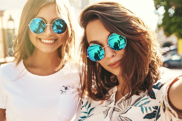 Zwei junge weibliche stilvolle Hippie-Brünette und blonde Frauen in Sommer-Hipster-Kleidung, die Selfie nehmen