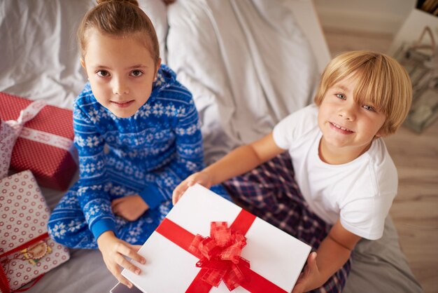Zwei Kinder sitzen auf Bett mit Weihnachtsgeschenk