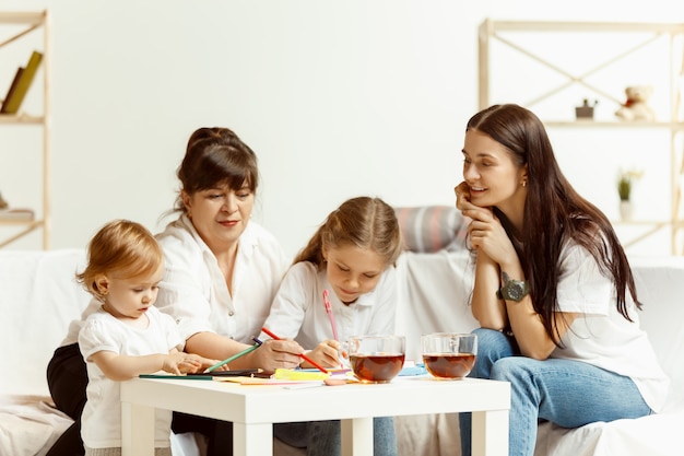 Zwei kleine Mädchen, ihre attraktive junge Mutter und ihre charmante Großmutter, sitzen auf dem Sofa und verbringen Zeit miteinander zu Hause. Generation von Frauen. Internationaler Frauentag. Schönen Muttertag.