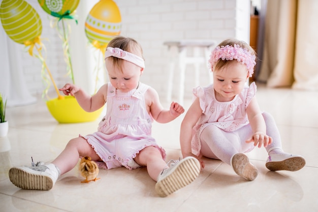 Zwei kleine Mädchen in rosa Kleidern spielen auf dem Boden im Studio mit Ostern Dekor