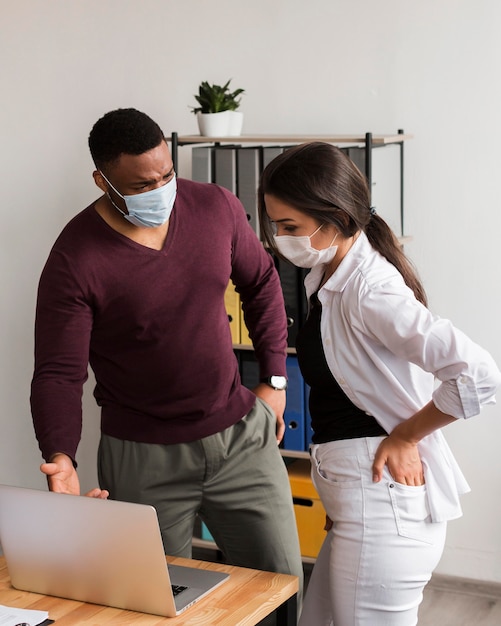 Zwei kollegen, die während einer pandemie mit masken im büro arbeiten