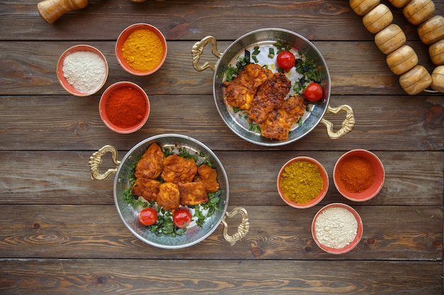 Zwei kupferfarbene Pfannen mit mariniertem Hähnchen, garniert mit Tomaten und Kräutern