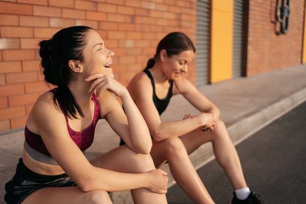 Zwei lachende Frauen vor dem städtischen Training. Mädchen, die sich auf das Laufen und Sitzen auf der Straße vorbereiten.