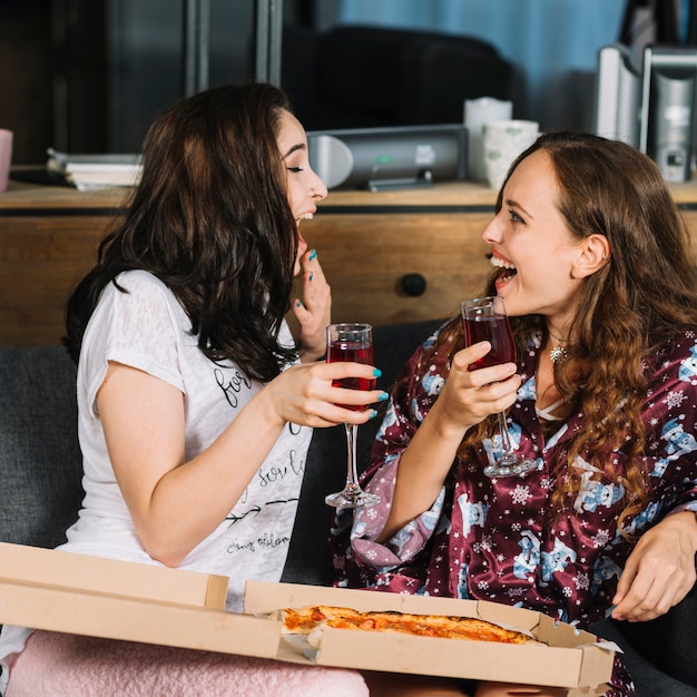 Kostenloses Foto zwei lachende freundinnen mit getränken und pizza