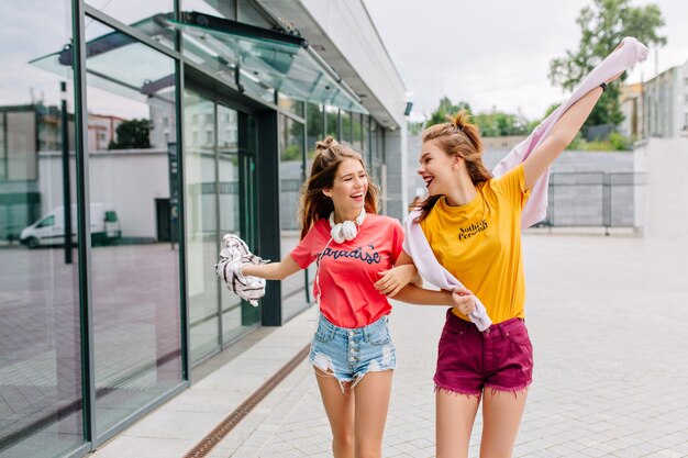 Zwei lächelnde Freunde gehen am Sommermorgen einkaufen und erzählen sich lustige Geschichten