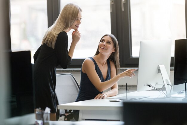 Zwei lächelnde Geschäftsfrauen, die mit Computer zusammen arbeiten