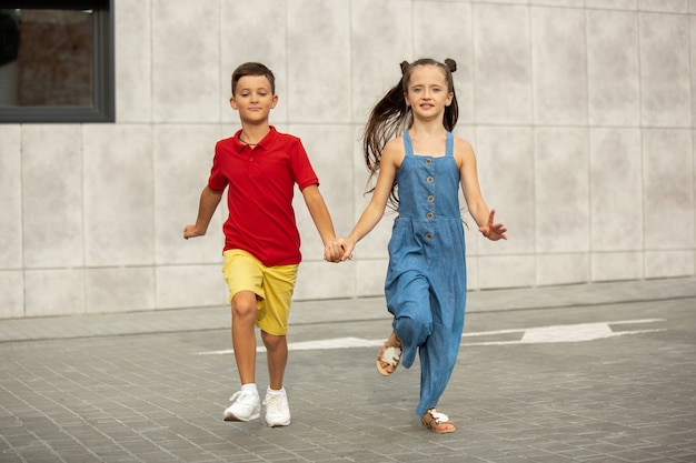 Zwei lächelnde kinder, junge und mädchen, die am sommertag zusammen in der stadt laufen?