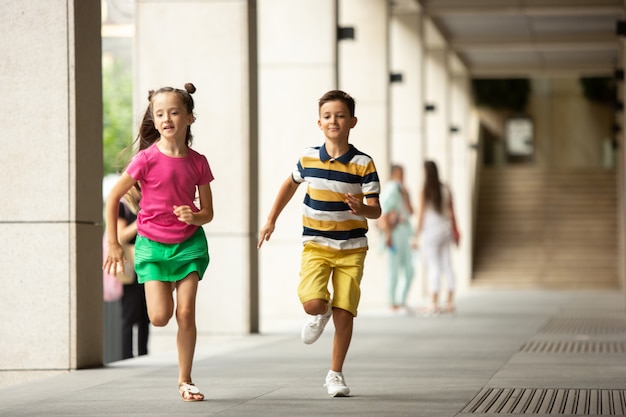 Zwei lächelnde Kinder, Junge und Mädchen, die zusammen in Stadt, Stadt am Sommertag laufen