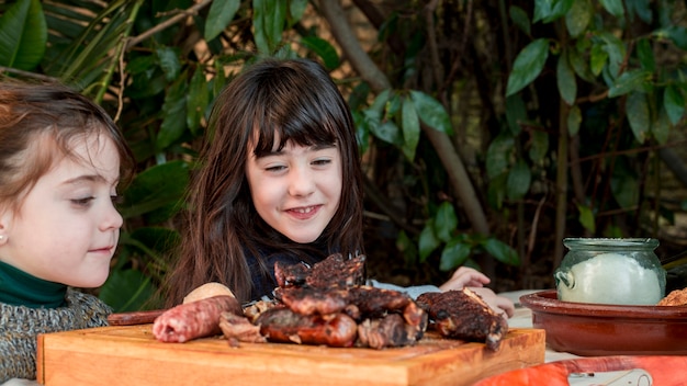 Zwei lächelnde mädchen, die gegrilltes fleisch auf hackendem brett betrachten