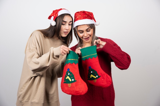 Zwei lächelnde Mädchen in Sankt-Hut, die Weihnachtssocken betrachten.