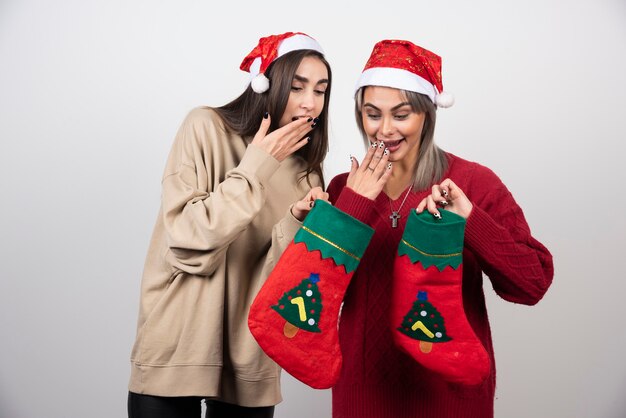 Zwei lächelnde Mädchen in Sankt-Hut, die Weihnachtssocken betrachten.