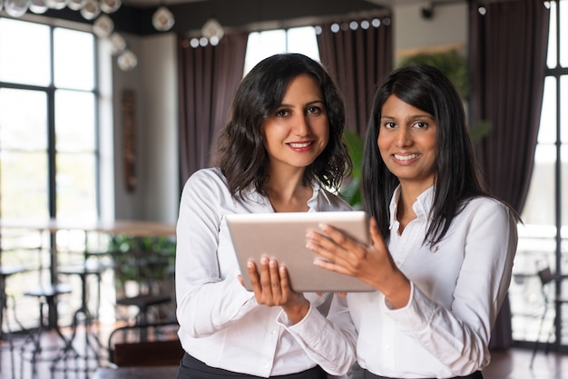 Zwei lächelnde weibliche Mitarbeiter, die Tablet-Computer im Café verwenden.