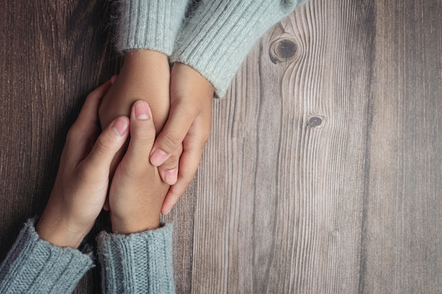 Zwei Leute, die Hände zusammen mit Liebe und Wärme auf Holztisch halten