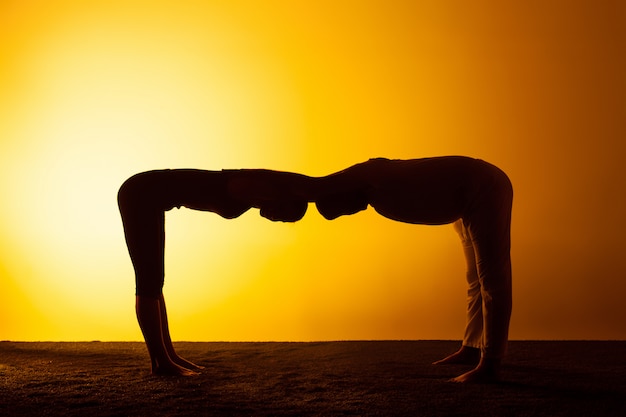 Kostenloses Foto zwei leute, die yoga im sonnenuntergangslicht praktizieren