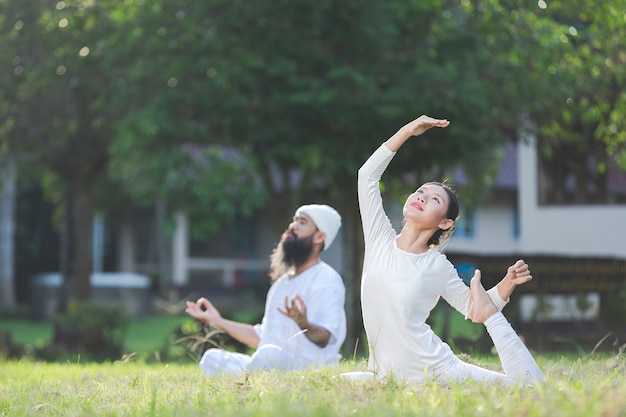 Zwei Leute im weißen Outfit, die Yoga in der Natur tun