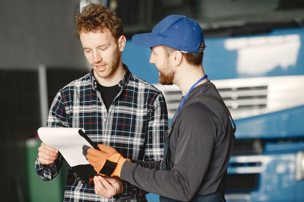 Kostenloses Foto zwei leute reden über arbeit. arbeit in der garage in der nähe von lkw. übermittlung von dokumenten mit waren