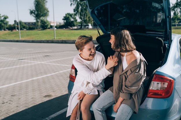 Zwei Mädchen auf dem Parkplatz am offenen Kofferraum posieren für die Kamera.