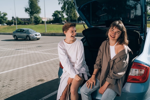 Kostenloses Foto zwei mädchen auf dem parkplatz am offenen kofferraum