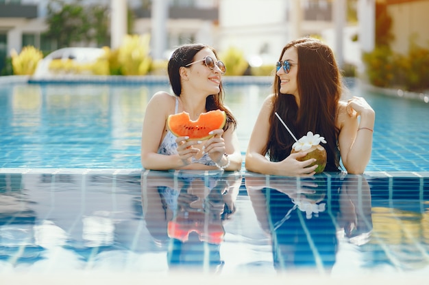 zwei Mädchen, die sich bräunen und Frucht am Pool haben