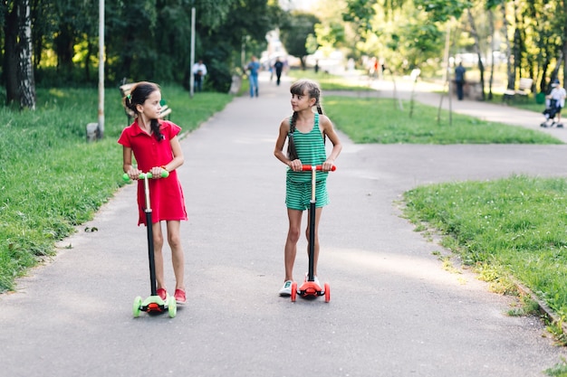 Zwei Mädchen, die Tretroller im Park reiten
