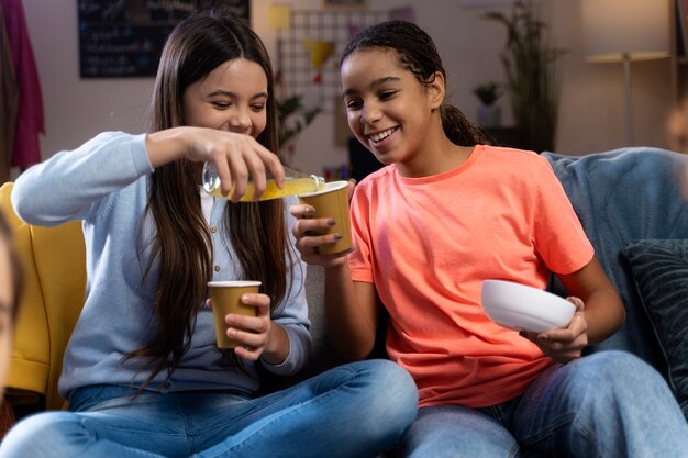 Zwei Mädchen im Teenageralter trinken zu Hause Soda aus Tassen und haben Spaß