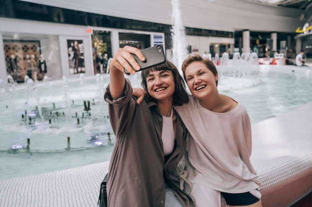 Zwei Mädchen machen ein Selfie im Einkaufszentrum neben einem Brunnen