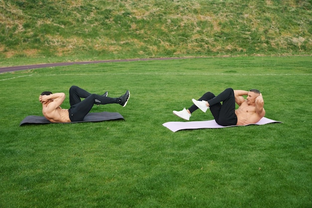 Zwei Männer mit nacktem Oberkörper machen Übungen für die Bauchmuskeln im Freien