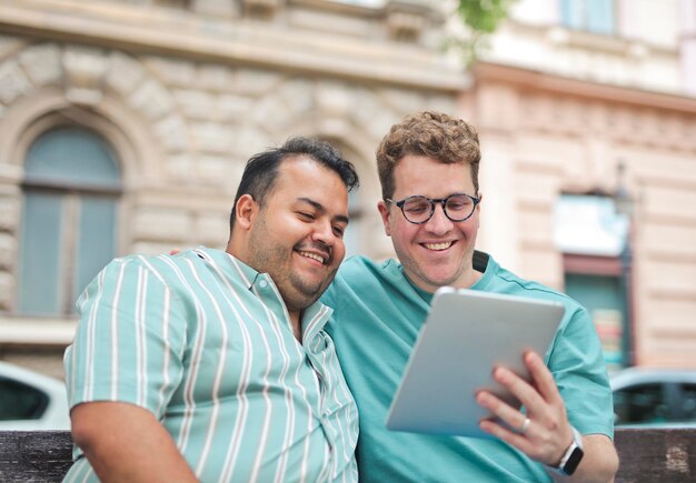 Zwei Männer umarmen sich auf einer Bank und benutzen ein Tablet