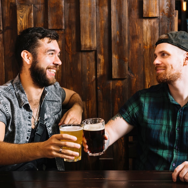 Zwei männliche Freunde, die mit Gläsern alkoholischen Getränken zujubeln