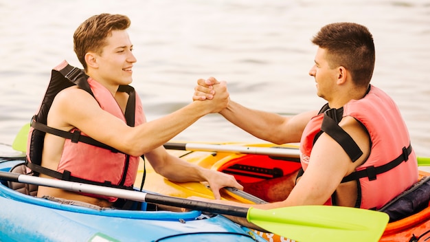 Zwei männliche Kayaker sitzend von Angesicht zu Angesicht, die Hand einander halten