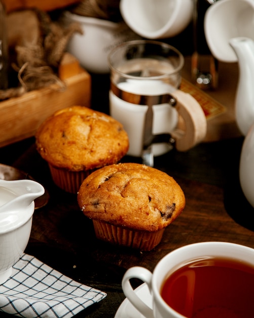 Zwei Muffins mit Rosinen, serviert mit schwarzem Tee