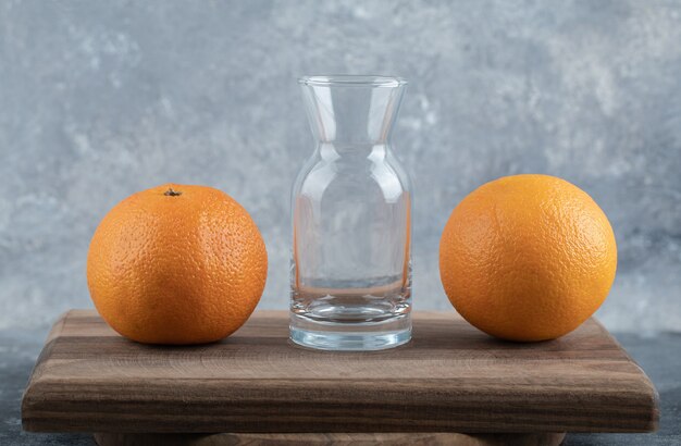 Zwei Orangen und Glas auf Holzbrett.