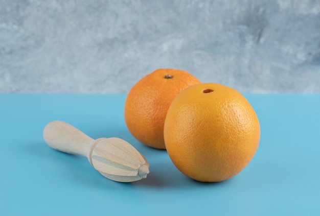 Zwei Orangen und hölzerne Reibahle auf blauem Tisch.