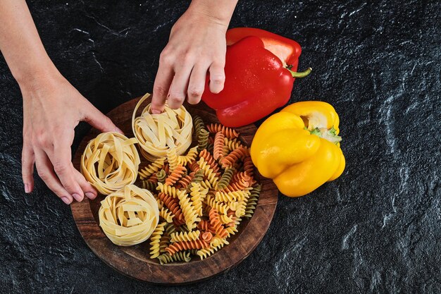 Zwei Paprika mit rohen Nudeln und ungekochten Makkaroni auf Schwarz.