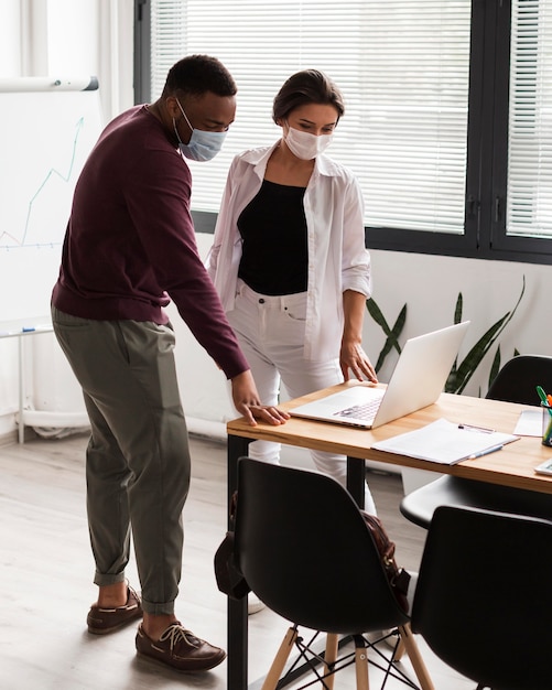 Kostenloses Foto zwei personen, die während einer pandemie im büro mit masken arbeiten