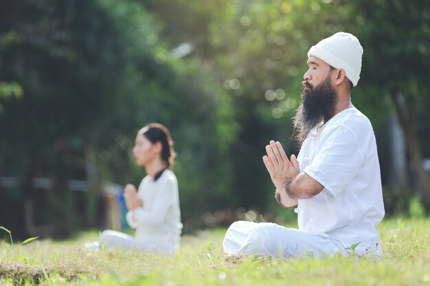 Zwei Personen im weißen Outfit meditieren in der Natur