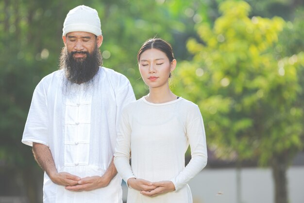 Zwei Personen im weißen Outfit meditieren in der Natur