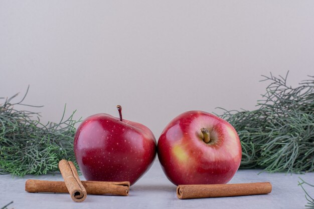 Zwei Äpfel und Zimtstangen unter Tannenzweigen auf weißem Hintergrund.