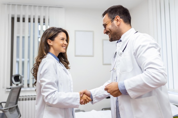 Zwei professionelle selbstbewusste Ärzte schütteln sich die Hände, während sie in der Klinik stehen