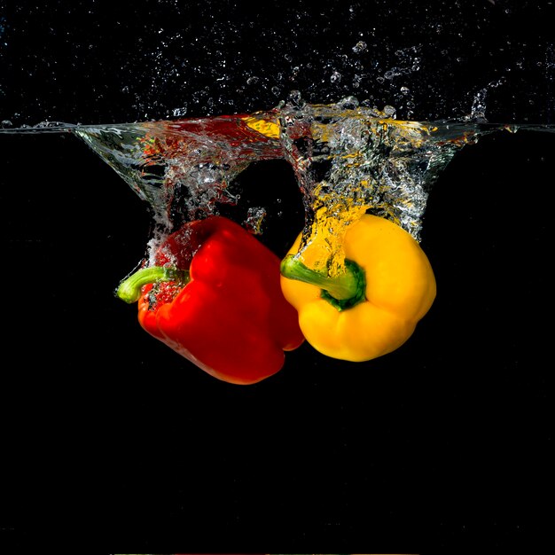 Zwei rote und gelbe Paprika spritzt in Wasser