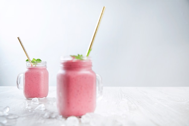 Zwei rustikale Gläser mit frisch gemischtem Smoothie aus Joghur, Beeren und Eis lokalisiert auf Holztisch und weißem Hintergrund