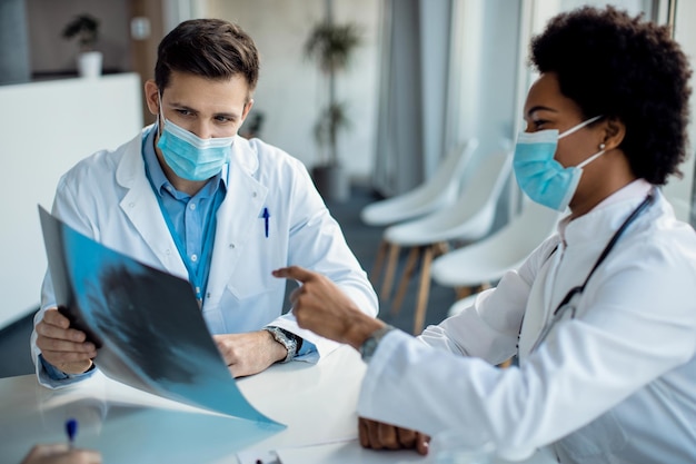 Zwei Ärzte mit Gesichtsmasken analysieren Röntgenaufnahmen eines Patienten im Krankenhaus