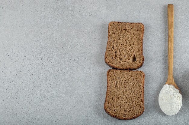 Zwei Scheiben Schwarzbrot mit Holzlöffel Mehl.