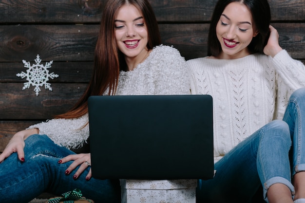 Zwei schöne frauen, die mit einem laptop auf dem boden sitzen